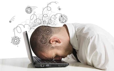 A frustrated man banging his head against his laptop computer.