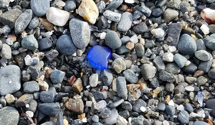 Smooth piece of wave tumbled blue sea glass washed up on pebbles at East Point Beach, Maine.