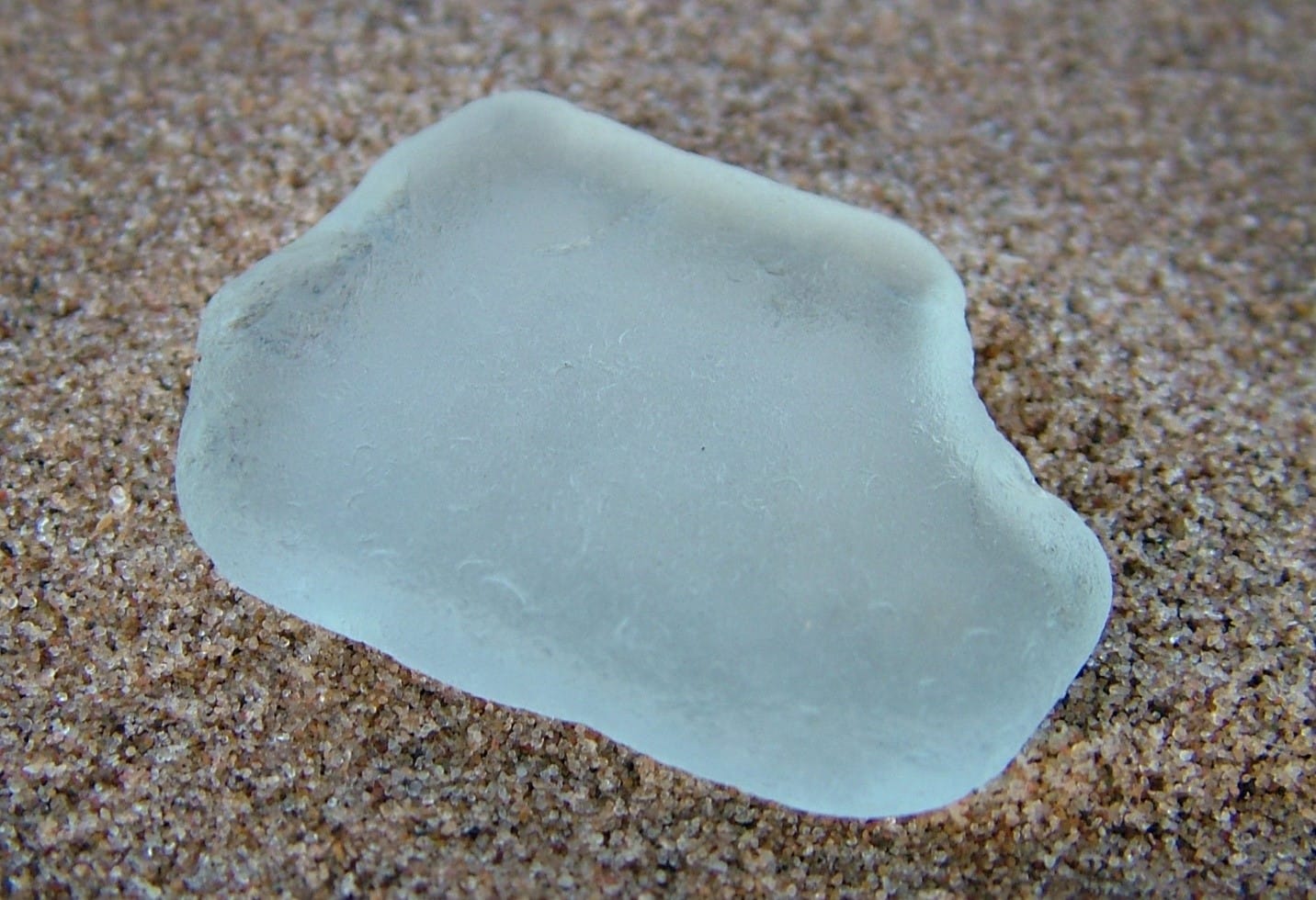 Frosted aqua sea glass laying on beach sand.