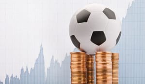 A football on top of coin stacks, with a profit graph in the background
