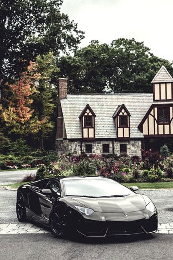 Matt black Lamborghini parked in the driveway of a mansion house.