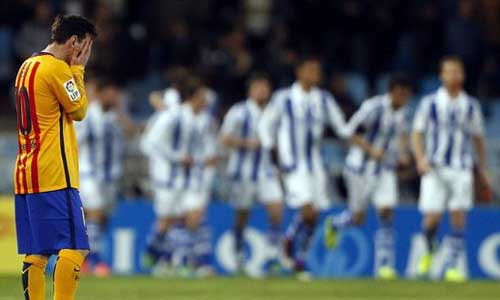 Real Socieadad players celebrate while Lionel Messi of Barcelona holds his head in his hands.