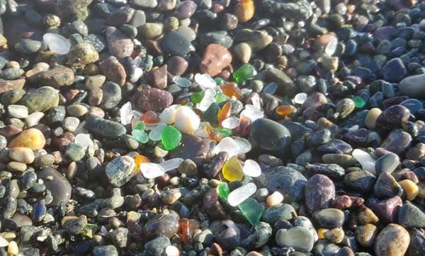 Sea glass in several colors such as green, brown, aqua sea glass, teal sea glass and clear sea glass on a pebbly beach at 40 Steps Beach in Nahant, Massachusetts.