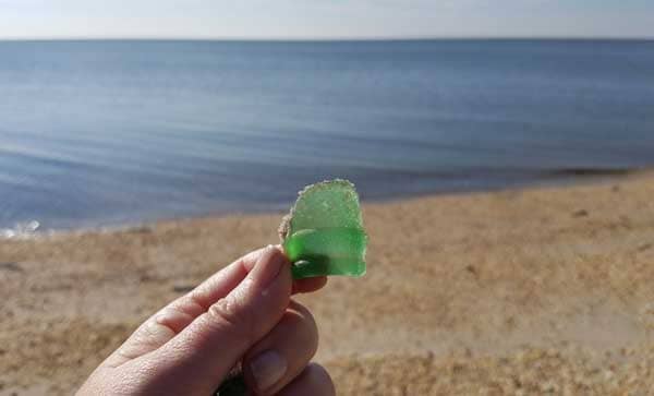 Hand holding a piece of smooth wave tumbled green sea glass on the beach in New Jersey.