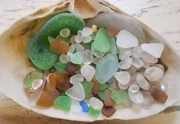 Clam shell full of green sea glass, aqua sea glass, brown sea glass and clear or white sea glass.