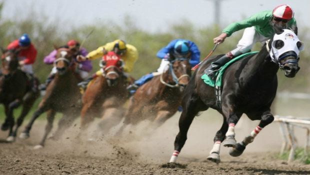 A number of jockeys ride their horses around a track in a horse racing event.