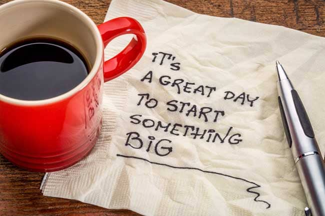 "It's a great day to start something big" written on a napkin next to a cup of coffee.