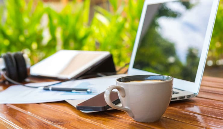 A desk with a laptop, cup to tea, pen and bookie slip on it