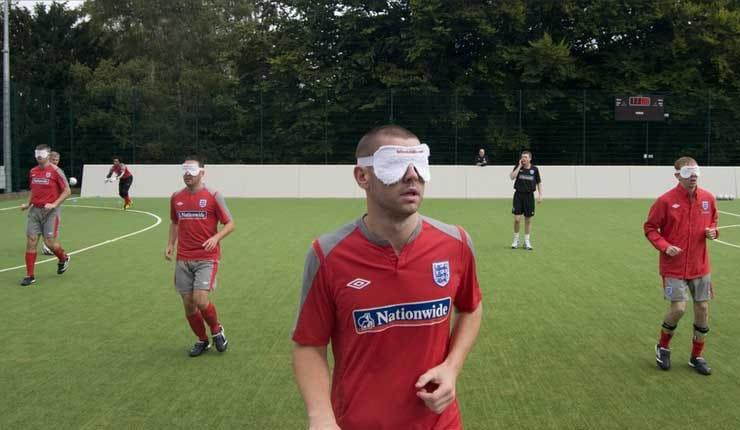 A game of blind football with players in red shirts, sponsored by Nationwide